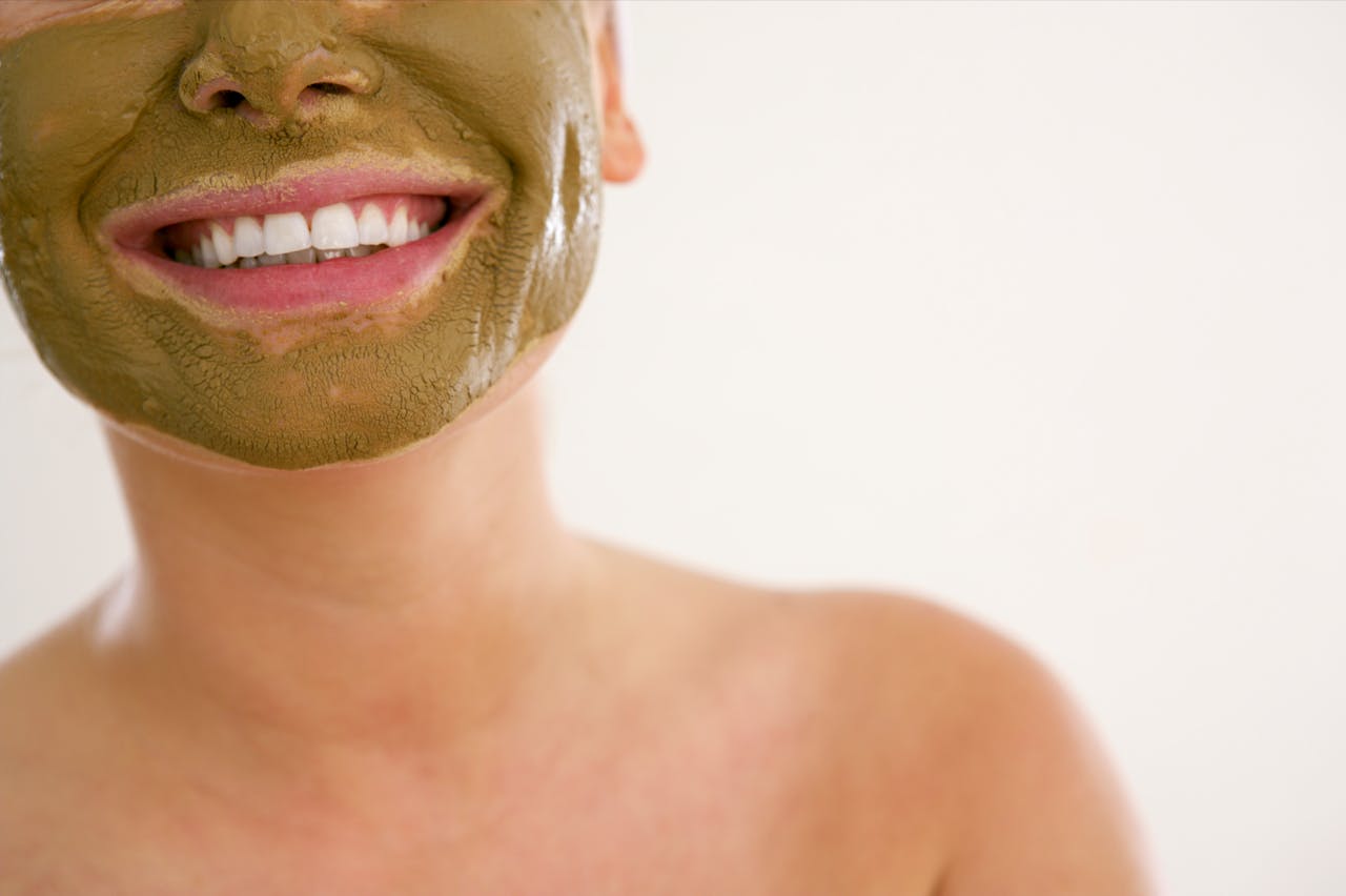 Close-up of a smiling woman applying a green cosmetic mask for skincare.