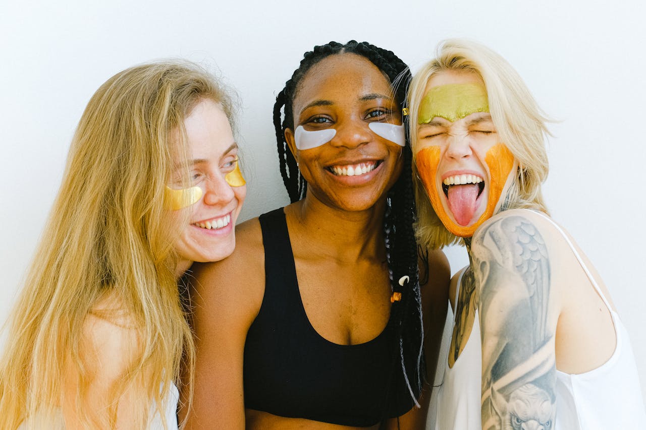 why-choose-us Three diverse women having fun with colorful skincare masks, embodying friendship and joy.